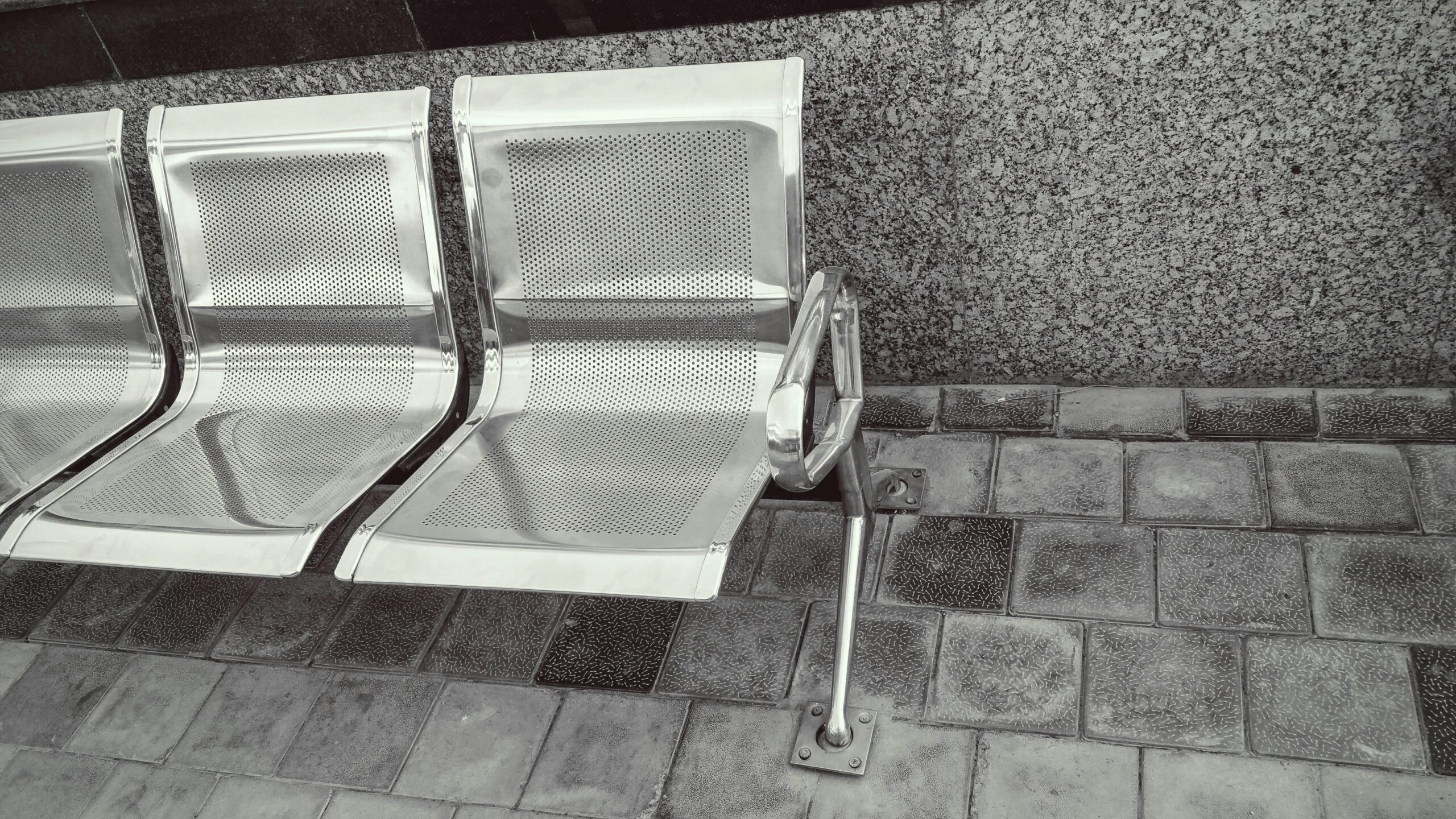 Modern stainless steel benches with granite wall and tile flooring in an outdoor setting.